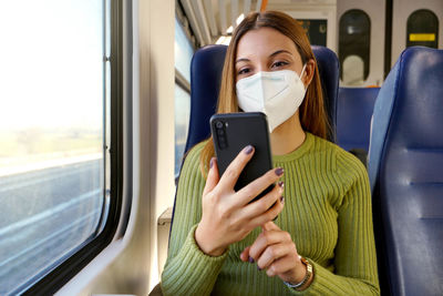 Train passenger using smartphone app during travel commute wearing protective face mask