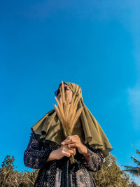 Low angle view of woman standing against blue sky