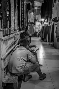 Rear view of man sitting on sidewalk in city