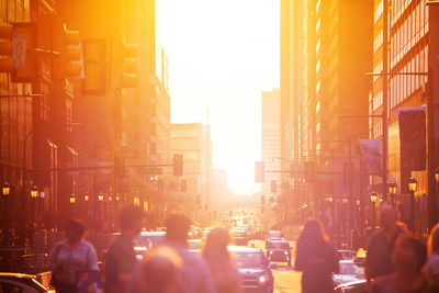 People on street amidst buildings in city during sunset