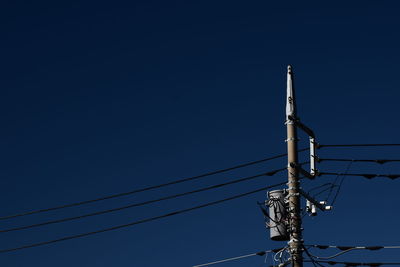 Low angle view of electricity pylon against clear blue sky