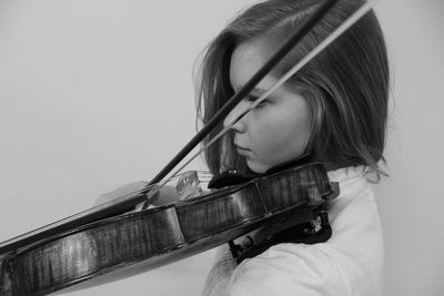 Woman playing violin while standing against wall