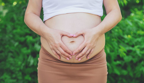 Pregnant woman making heart shape gesture on stomach