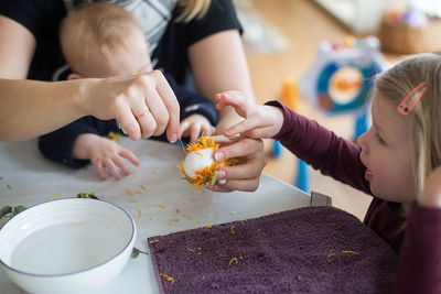 Midsection of woman with children making easter egg with petals