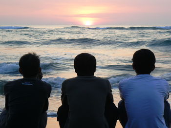 Rear view of men on beach against sky during sunset