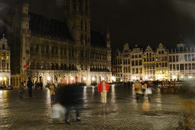 People in illuminated city against sky at night