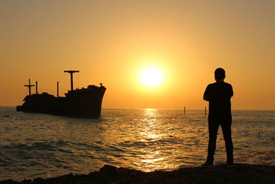 Silhouette men standing on shore against sky during sunset