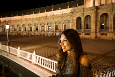 Thoughtful young woman standing against historic building at night