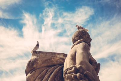 Low angle view of birds perching on statue against sky
