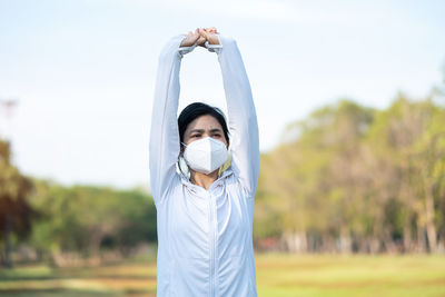 Woman wearing mask with arms raised standing at park