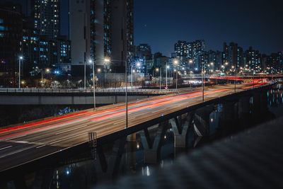 Light trails on road by illuminated buildings in city at night