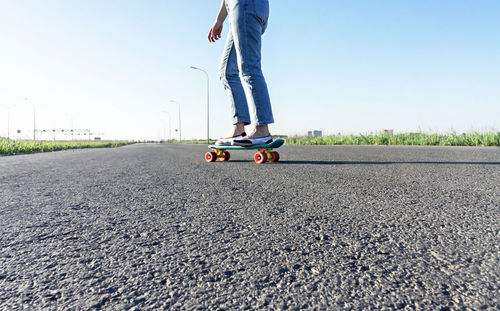 Skater caucasian young woman legs in blue jeans skateboarding on road in summer, outdoor activities