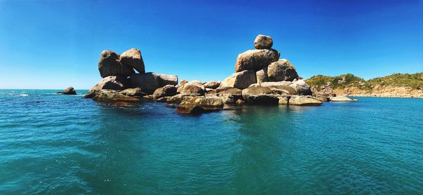 View of rock formation in sea against clear blue sky