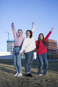 Portrait of smiling friends with hand raised standing in city
