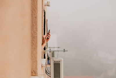 Cropped hands of woman using smart phone outside window