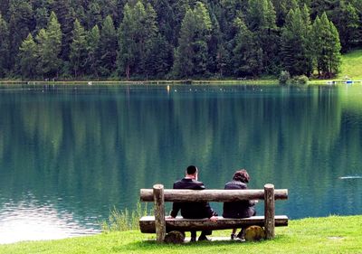 Rear view of men sitting on bench by lake