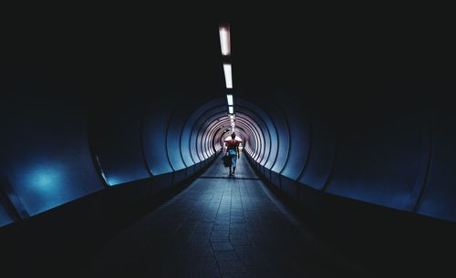 Rear view full length of woman walking in illuminated tunnel