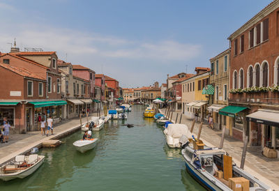 Boats in canal amidst buildings in city against sky