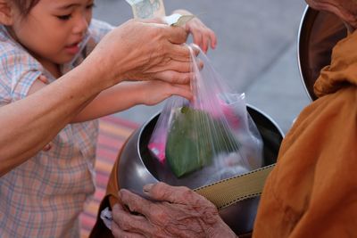 Close-up of parent with daughter giving food to monk