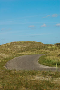 Road amidst field against blue sky