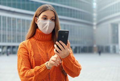 Portrait of young woman using phone while standing in city