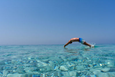 Man diving in sea against clear blue sky