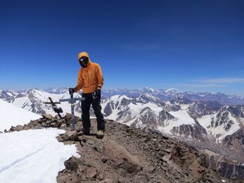 Rear view of man standing on snowcapped mountain against blue sky