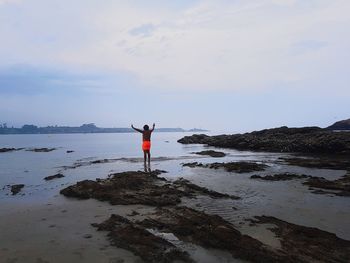 Rear view of man standing on beach against sky