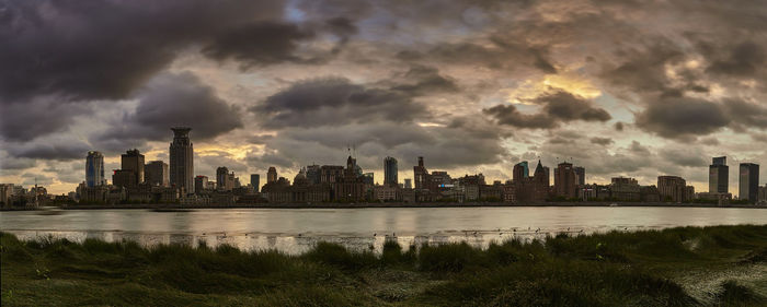 City at waterfront against cloudy sky