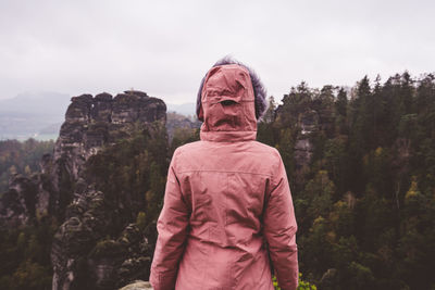 Rear view of woman standing on cliff against landscape