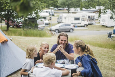 Happy family talking while having food together at table by tent