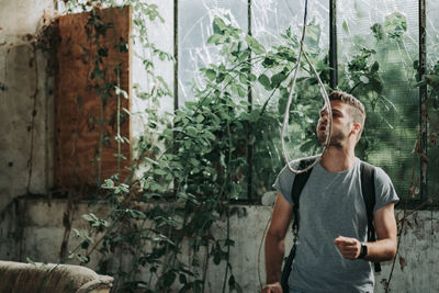 Young man looking at rope while standing by plants