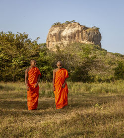 Rear view of men standing on rock against sky