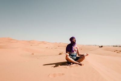 A man in a turban meditating on a dune in the sahara desert