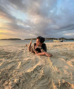 Rear view of woman exercising at beach against sky during sunset