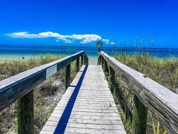 Walkway by sea against blue sky