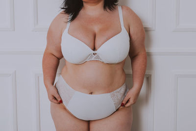 Midsection of young woman standing against white wall