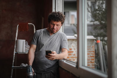Young man with a smartphone at the window.