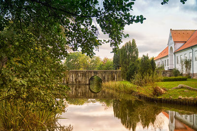 Arch bridge over canal amidst trees and buildings against sky