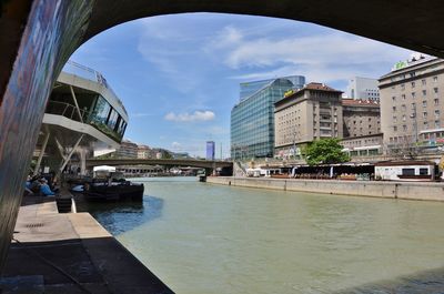 Bridge over river by buildings in city against sky