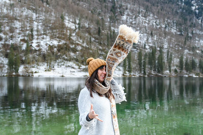 Young woman in winter sweater smiling, standing by a lake.