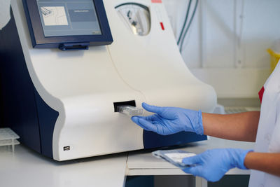 Side view of crop unrecognizable female medical specialist putting tube into analyzer while making diagnostic in laboratory