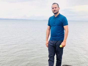 Young man standing at beach against sky