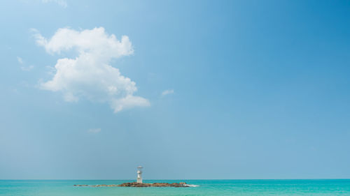 A lighthouse standing alone in the wide ocean in blue sky fluffy white clouds with sunlight shines