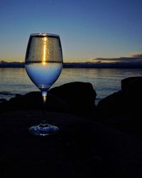 Glass of water by sea against sky during sunset