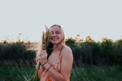 Portrait of smiling young woman standing on land against sky