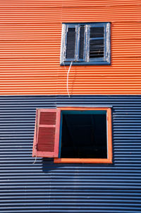 Low angle view of window with shutter on two tone corrugated iron building.