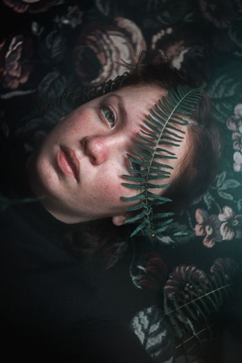 Close-up high angle portrait of young woman lying on pillow with plant