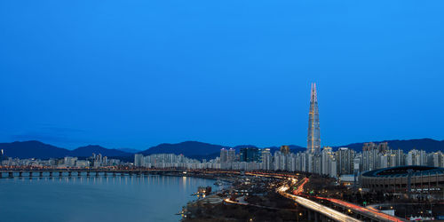 Illuminated buildings in city against clear blue sky