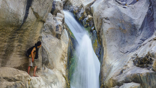 Full length of man standing on rock by waterfall